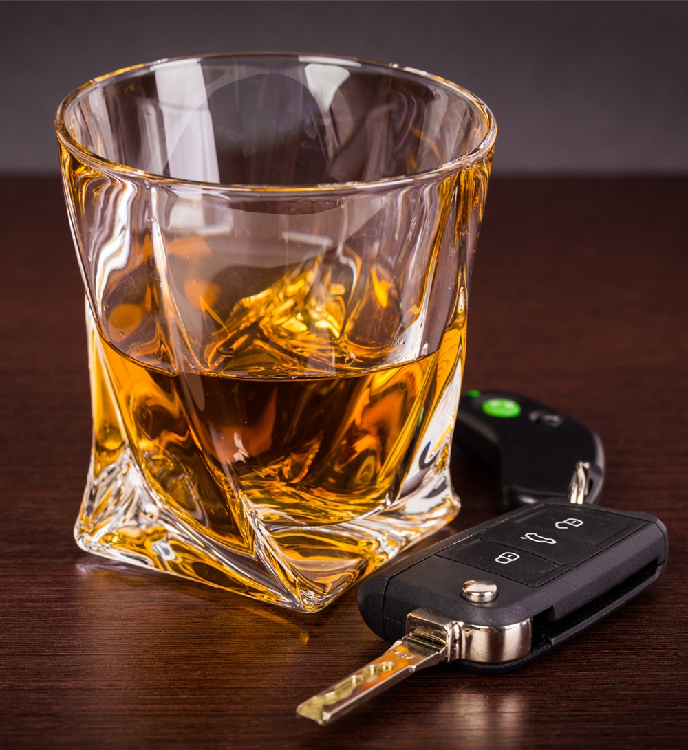 Car keys sit on a table next to a glass of liquor