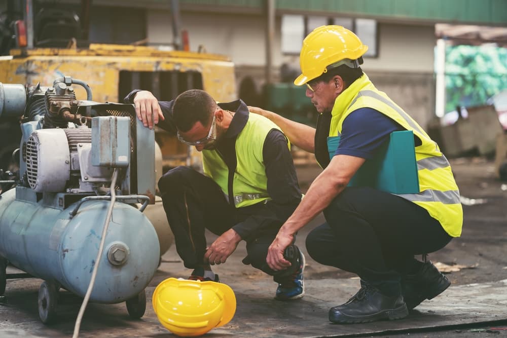 Injured construction worker receiving assistance from a coworker at a job site after a workplace accident involving heavy equipment.